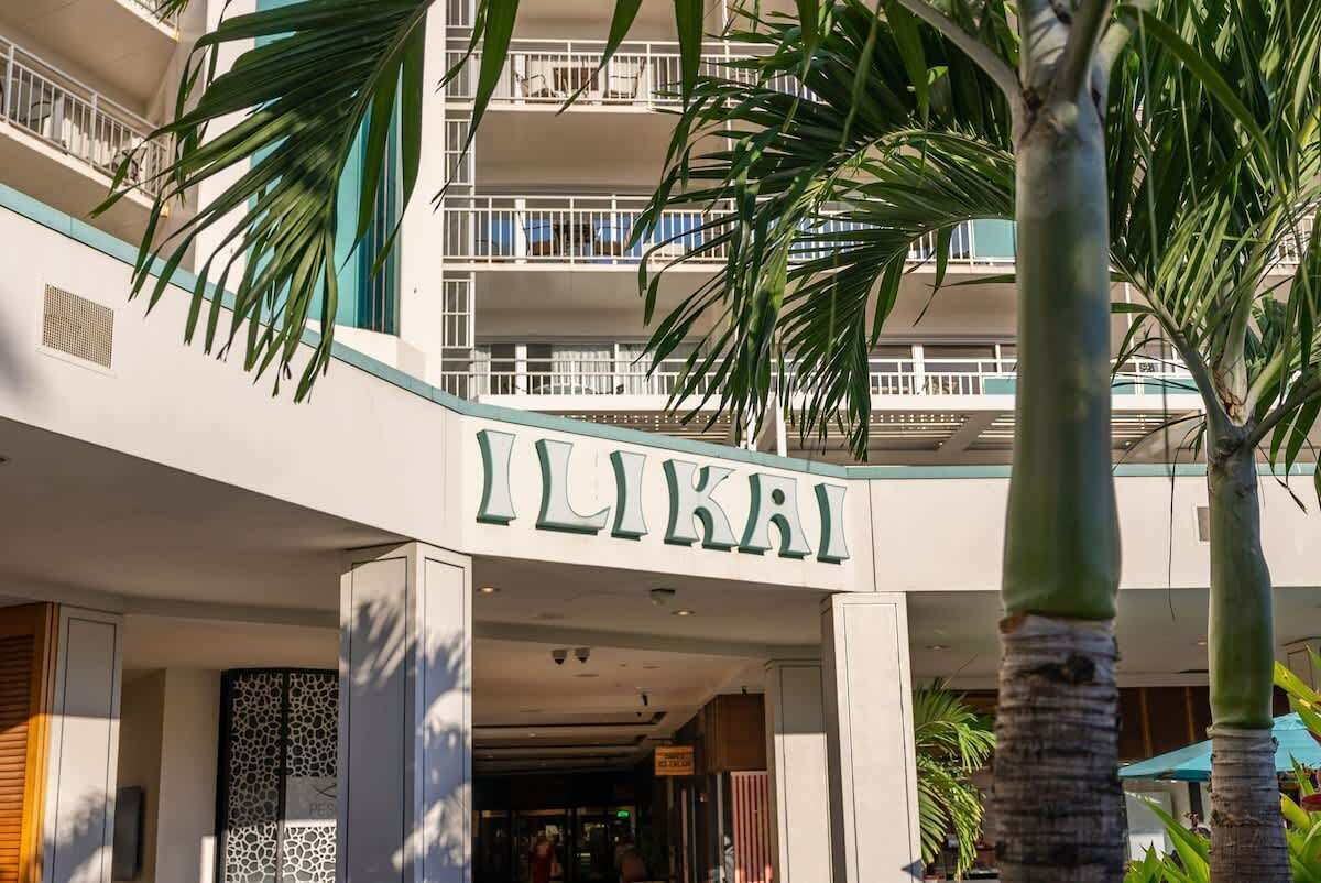 Ein Hotel Eingang mit einem Schild mit der Aufschrift 'ILIKAI' und einem modernen architektonischen Design, inklusive Balkone und Palmen.