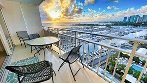 A balcony with a table and chairs, overlooking a marina with boats and a cityscape. - @ Marbella Lane – Dreamy Sunset Views by the Sea (Honolulu)