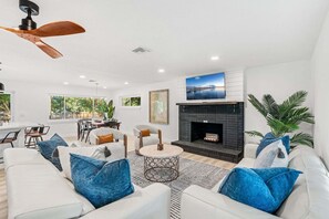 A modern living room with a fireplace, white sofas, a coffee table, and a ceiling fan. - 502 Colony Street (Melbourne Beach)