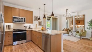 A modern kitchen with wooden cabinets, stainless steel appliances, pendant lighting, and a view to a dining area.