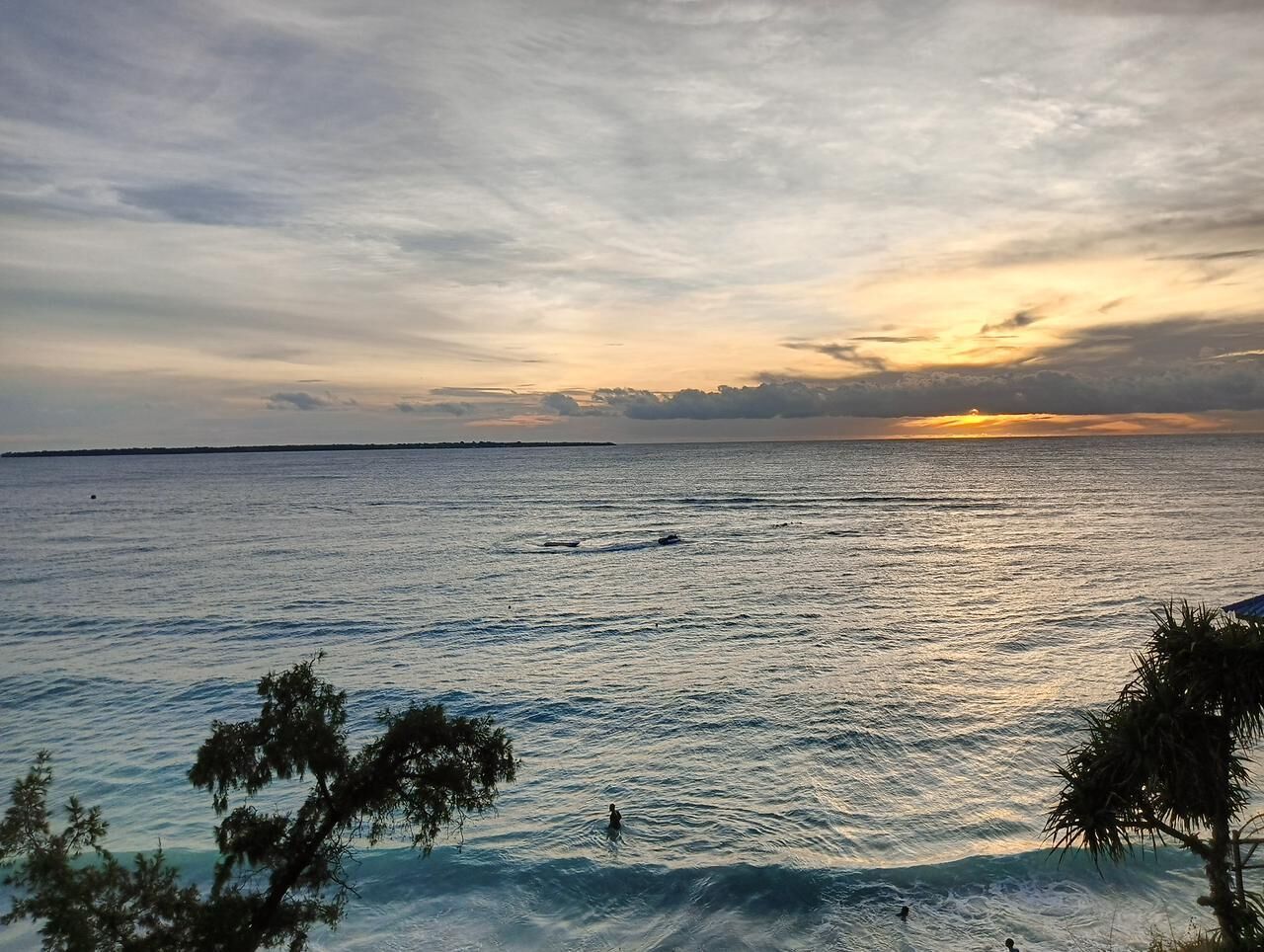 Une vue sur la plage, avec une eau calme, un coucher de soleil et une côte lointaine.