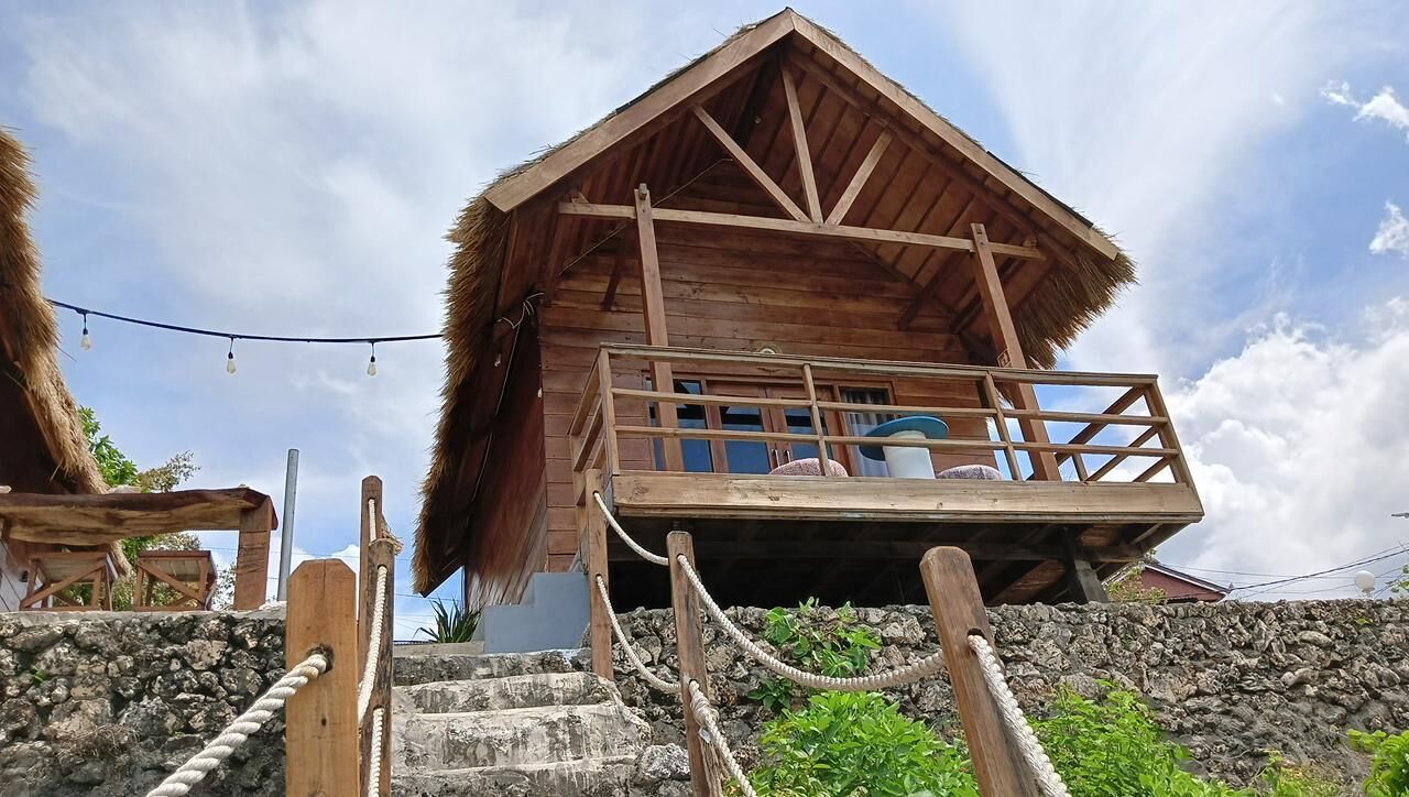 A wooden cabin with a thatched roof, a balcony, and a stone staircase leading up to it.