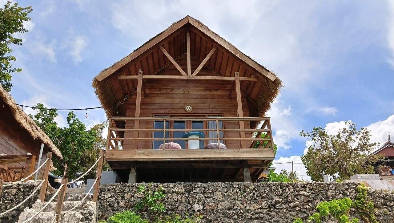 A wooden building with a balcony, a stone wall in front, and a thatched roof.