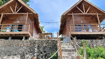 Dos cabañas de madera con techos de paja, cada una con un balcón y una pequeña mesa.