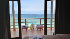 Un balcón con vista al océano, dos mesas redondas y una terraza de madera.