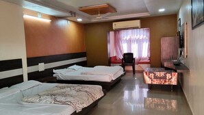 Habitación de hotel con tres camas, televisión, escritorio y una silla.