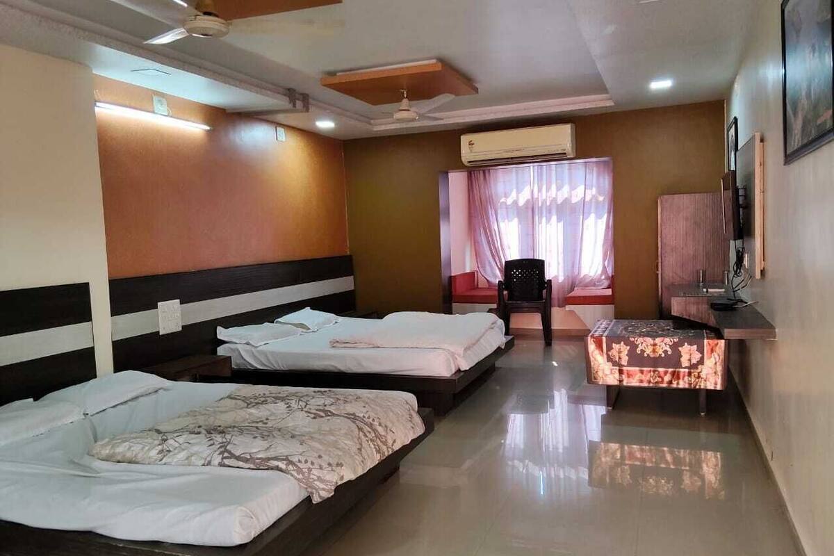 Habitación de hotel con tres camas, televisión, escritorio y una silla.
