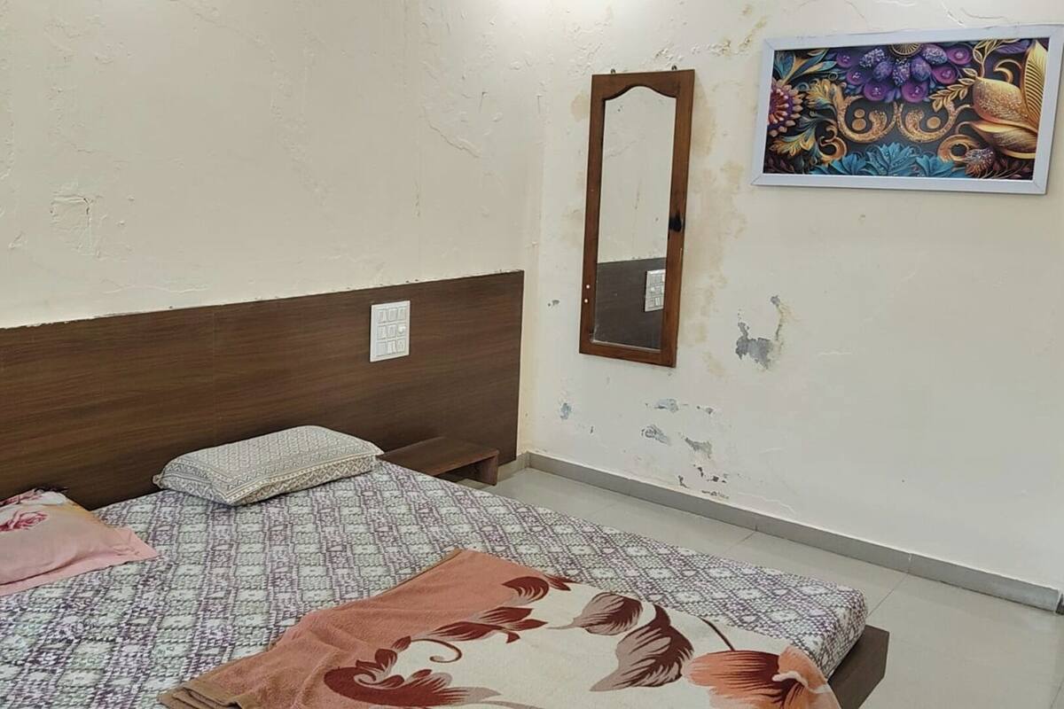 Una habitación pequeña y sencilla con una cama individual, una mesita de noche, un espejo y un cuadro colgado en la pared.