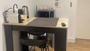 A compact kitchen with a microwave, toaster, and coffee maker on the counter, a TV mounted on the wall, and a door with a sensor. - On the road to the castles (Soussans)