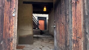 Una escalera de madera rústica que lleva a una habitación con piso de piedra y una lámpara colgante.