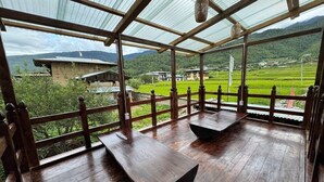 Una terraza cubierta de madera con bancos que da a un paisaje verde y edificios a la distancia.