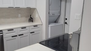 A modern kitchen with white cabinetry, a built-in dishwasher, and a black induction cooktop. - Newly renovated home near TMC, Downtown, UH, TSU available for short term rental (Houston)