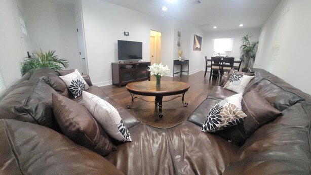 A living room with a brown leather sofa, a coffee table with a vase of flowers, and a dining area with a table and chairs. - Newly renovated home near TMC, Downtown, UH, TSU available for short term rental (Houston)