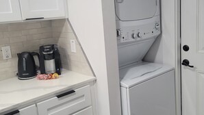 A compact kitchen with white cabinetry, a coffee maker, and a stacked washer and dryer. - Newly renovated home near TMC, Downtown, UH, TSU available for short term rental (Houston)