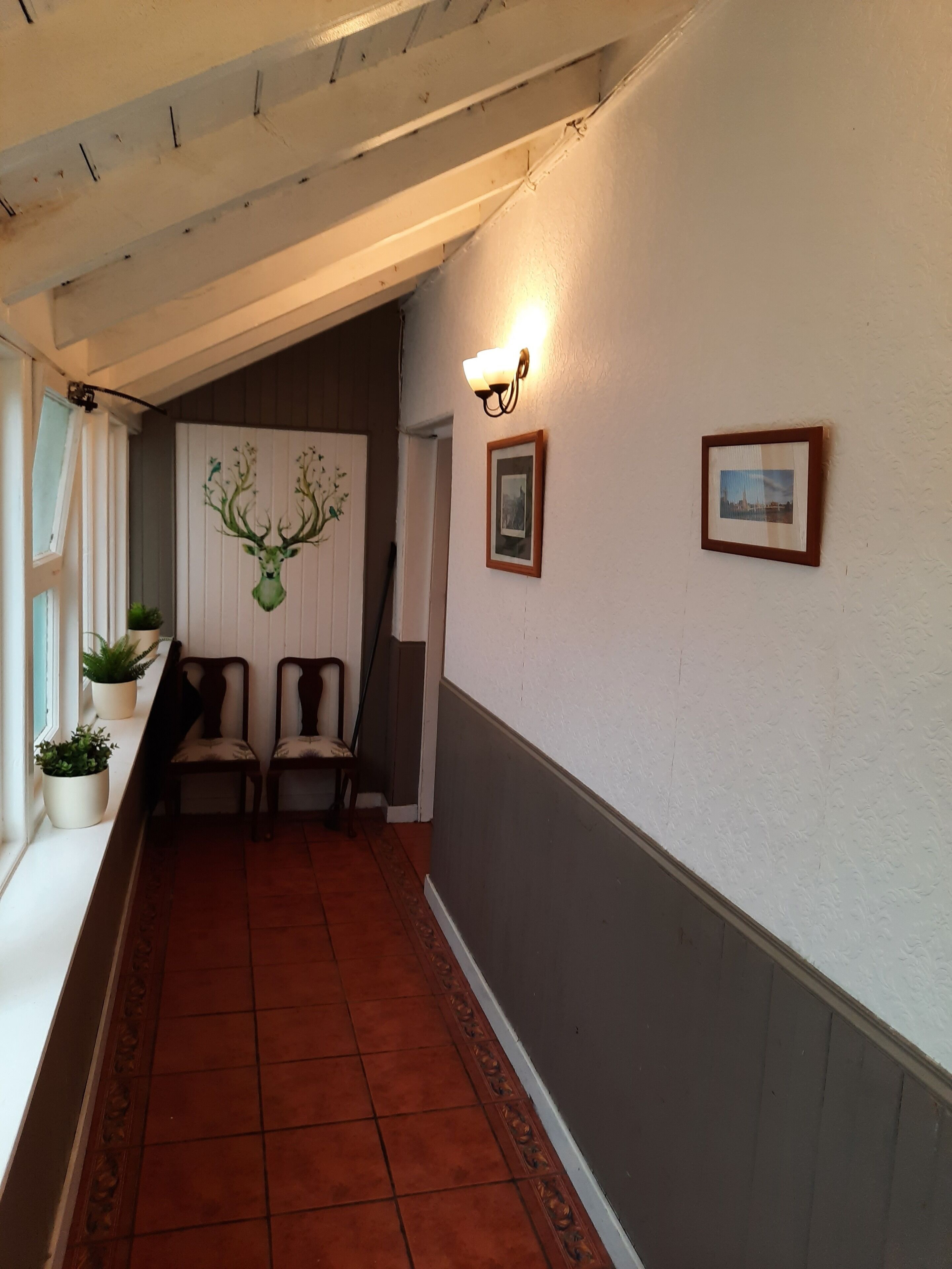 A hallway with a tiled floor, a wall-mounted picture frame, and a wall-mounted light fixture.