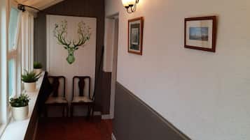 A hallway with a tiled floor, a wall-mounted picture frame, and a wall-mounted light fixture.