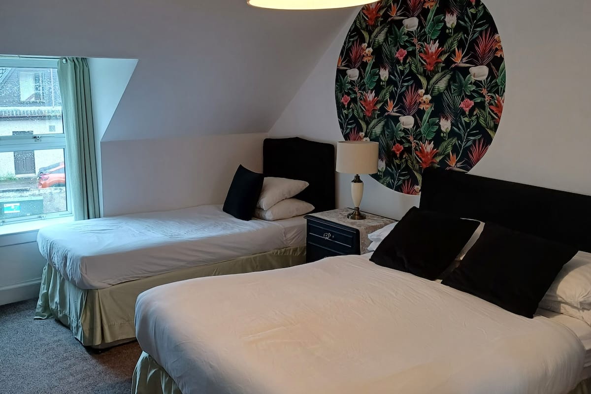A hotel room with two beds, a round wall decoration, a ceiling light, and a window with curtains.