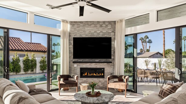 A modern living room with a fireplace, large TV, and a pool view. - Desert Oasis: Pool, Spa, Golf Sim & Family Fun! (Bermuda Dunes)