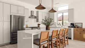 A modern kitchen with stainless steel appliances, a central island with bar stools, and pendant lighting. - Desert Oasis: Pool, Spa, Golf Sim & Family Fun! (Bermuda Dunes)