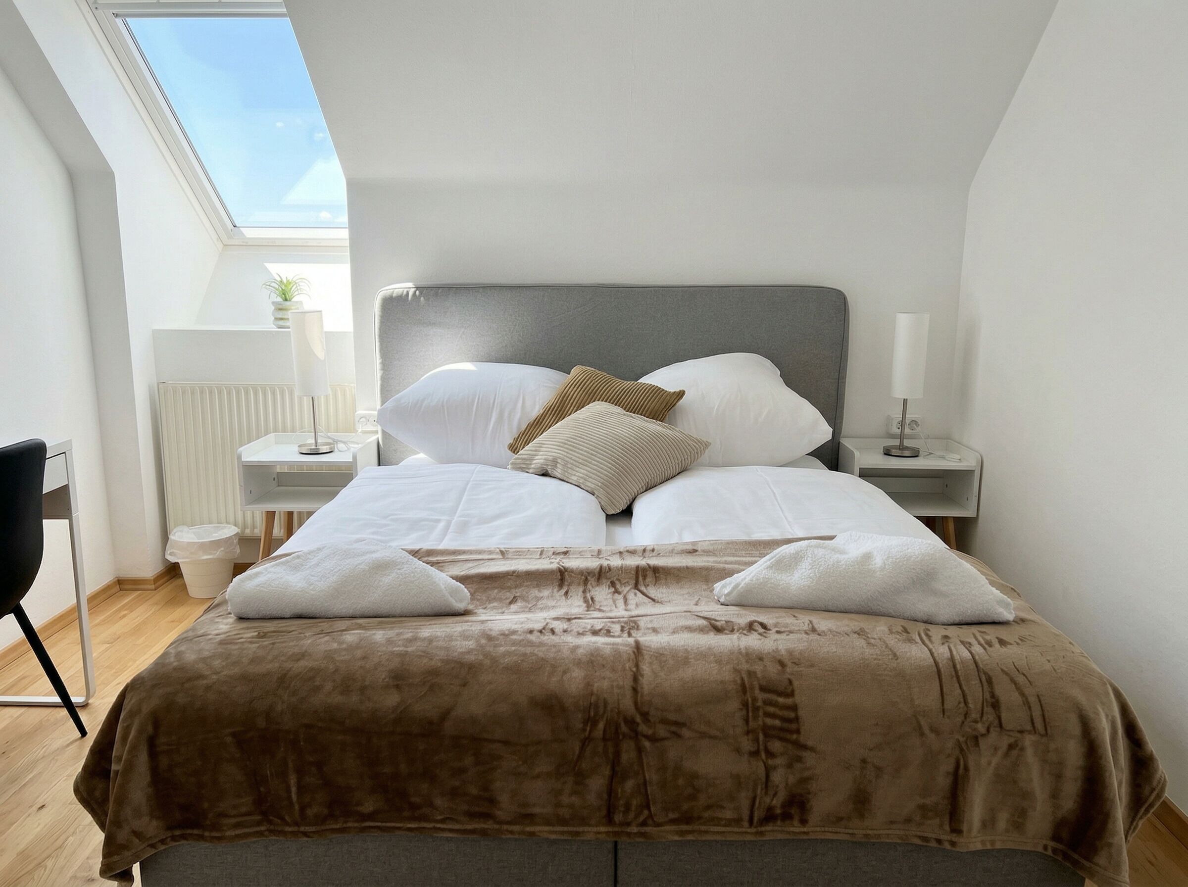 A bedroom with a bed, bedside tables, a chair, a radiator, and a skylight.