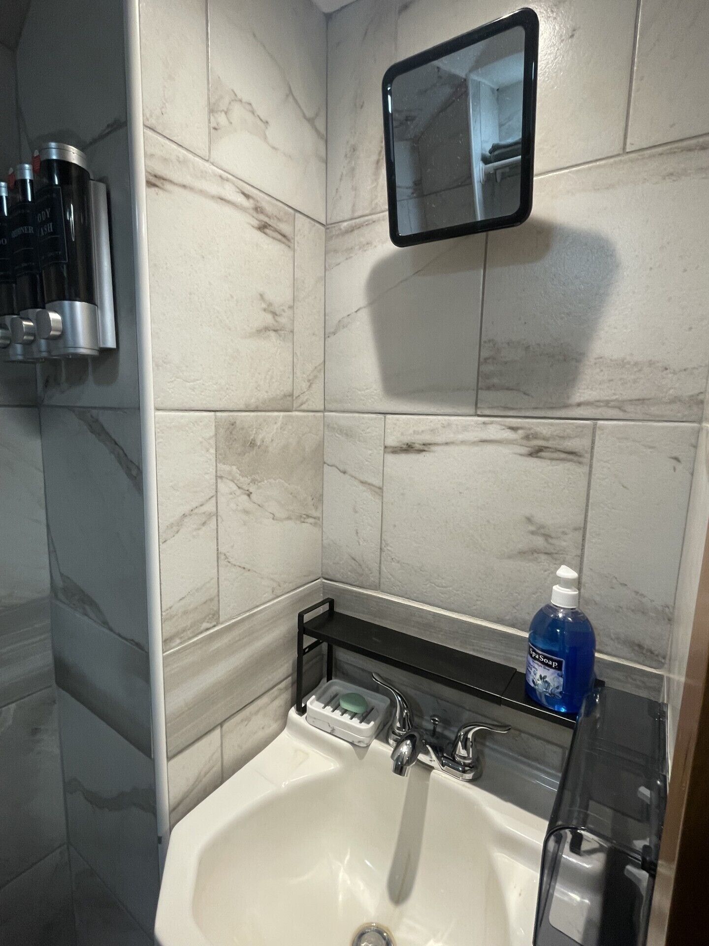 Une salle de bain avec un lavabo blanc, un miroir et une étagère contenant des articles de toilette.