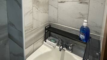 Une salle de bain avec un lavabo blanc, un miroir et une étagère contenant des articles de toilette.