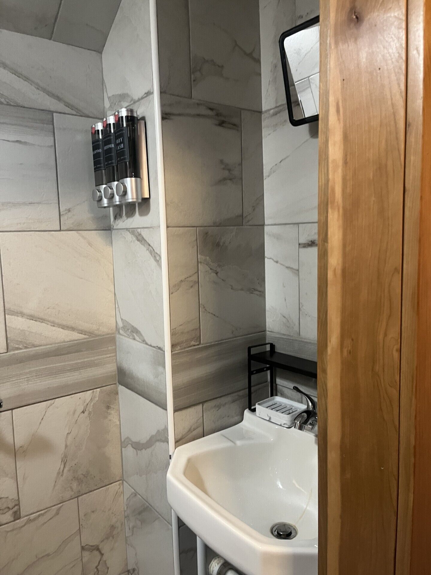 A bathroom with a marble-tiled wall, a white sink, and a wooden door.