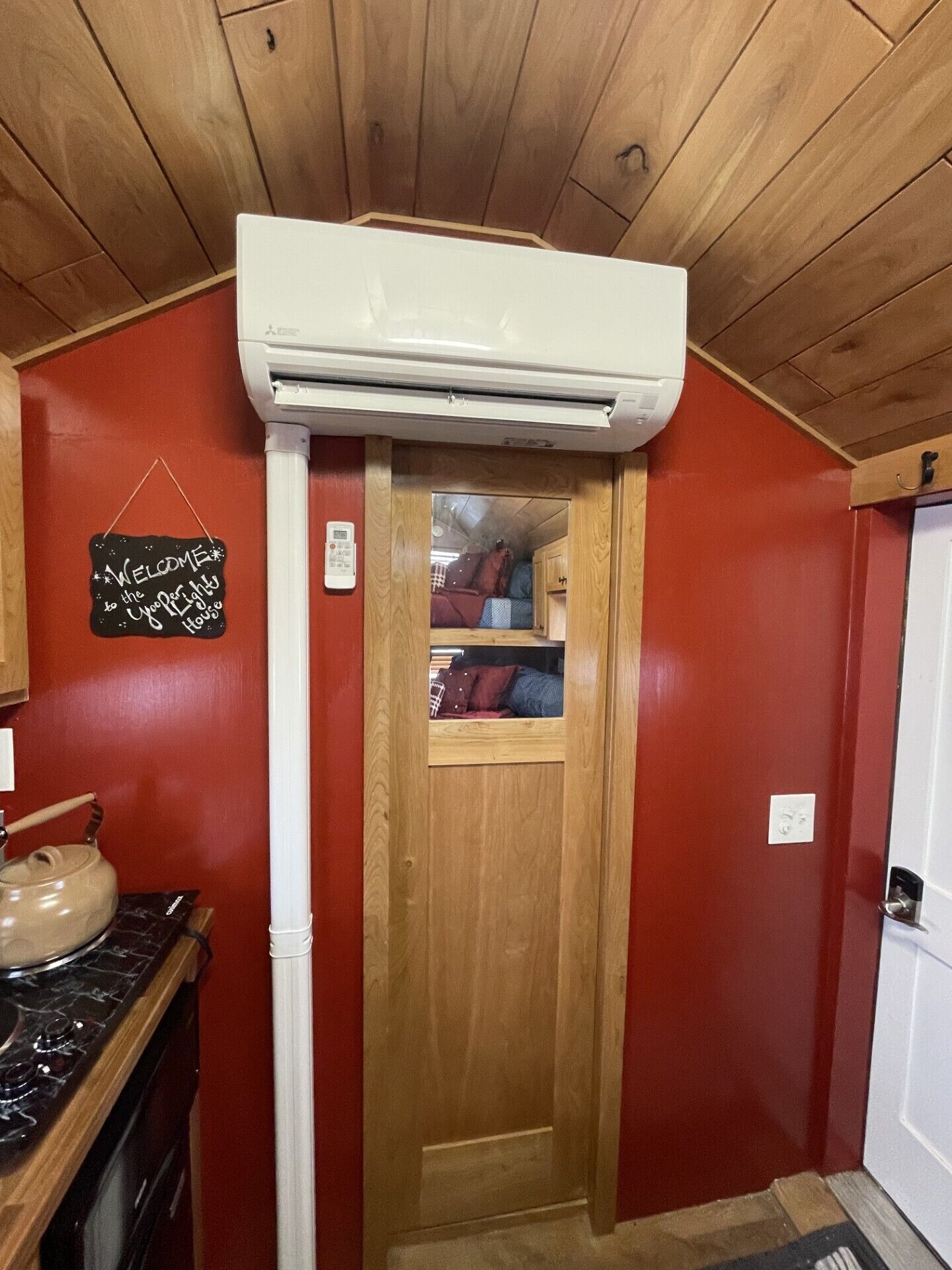 Una cocina compacta con estufa integrada, una puerta de madera que da a un espacio de almacenamiento y un equipo de aire acondicionado blanco instalado en el techo.