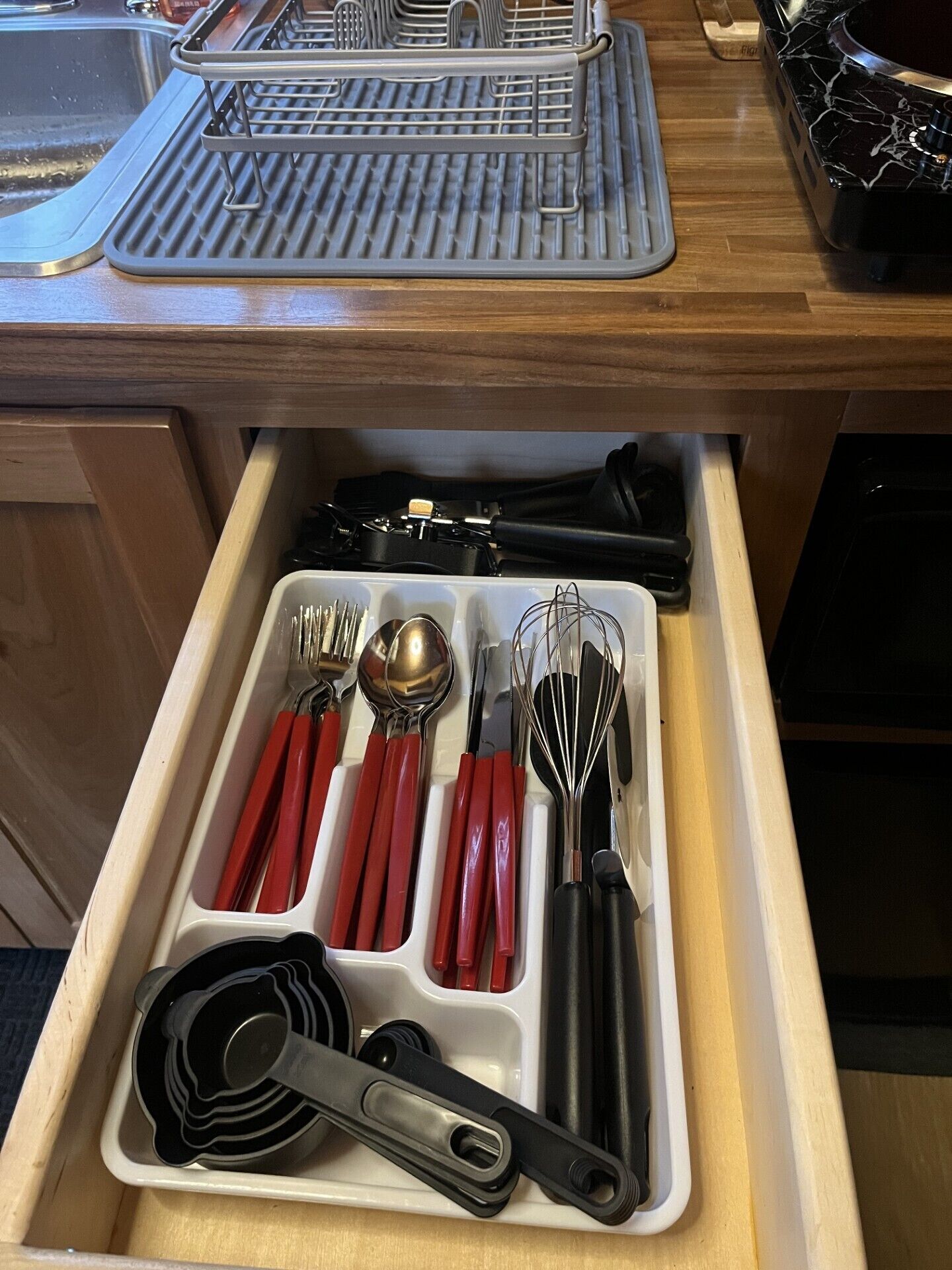 A kitchen drawer with utensils and a grater.