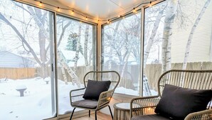A cozy room with two wicker chairs, a small round table, and a large window overlooking a snowy yard. - Elegant Linden Hills Home, Family Friendly, Walk to Lake, Dining, and Shopping (Minneapolis)