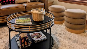 A cozy living room with a brown leather sofa, a round black coffee table with a wicker basket, and a magazine. There are ottomans and a lamp in the room. - Elegant Linden Hills Home, Family Friendly, Walk to Lake, Dining, and Shopping (Minneapolis)
