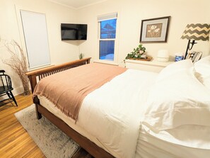 A bedroom with a bed, a TV mounted on the wall, a window, a bedside table with a lamp, and a chair. - Elegant Linden Hills Home, Family Friendly, Walk to Lake, Dining, and Shopping (Minneapolis)