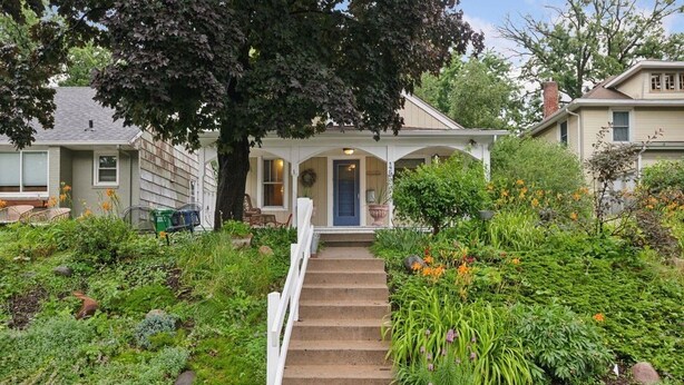 A house with a front porch, a staircase leading to the entrance, and a garden with various plants and flowers. - Elegant Linden Hills Home, Family Friendly, Walk to Lake, Dining, and Shopping (Minneapolis)