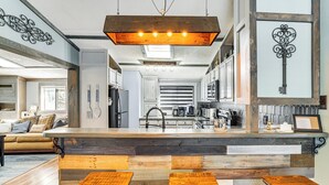 Una cocina moderna con una barra de madera, dos taburetes y una lámpara colgante.