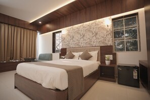 A modern bedroom with a large bed, a bedside table, a nightstand, a small potted plant, and a built-in TV. - High Five Hotels (Assagao)