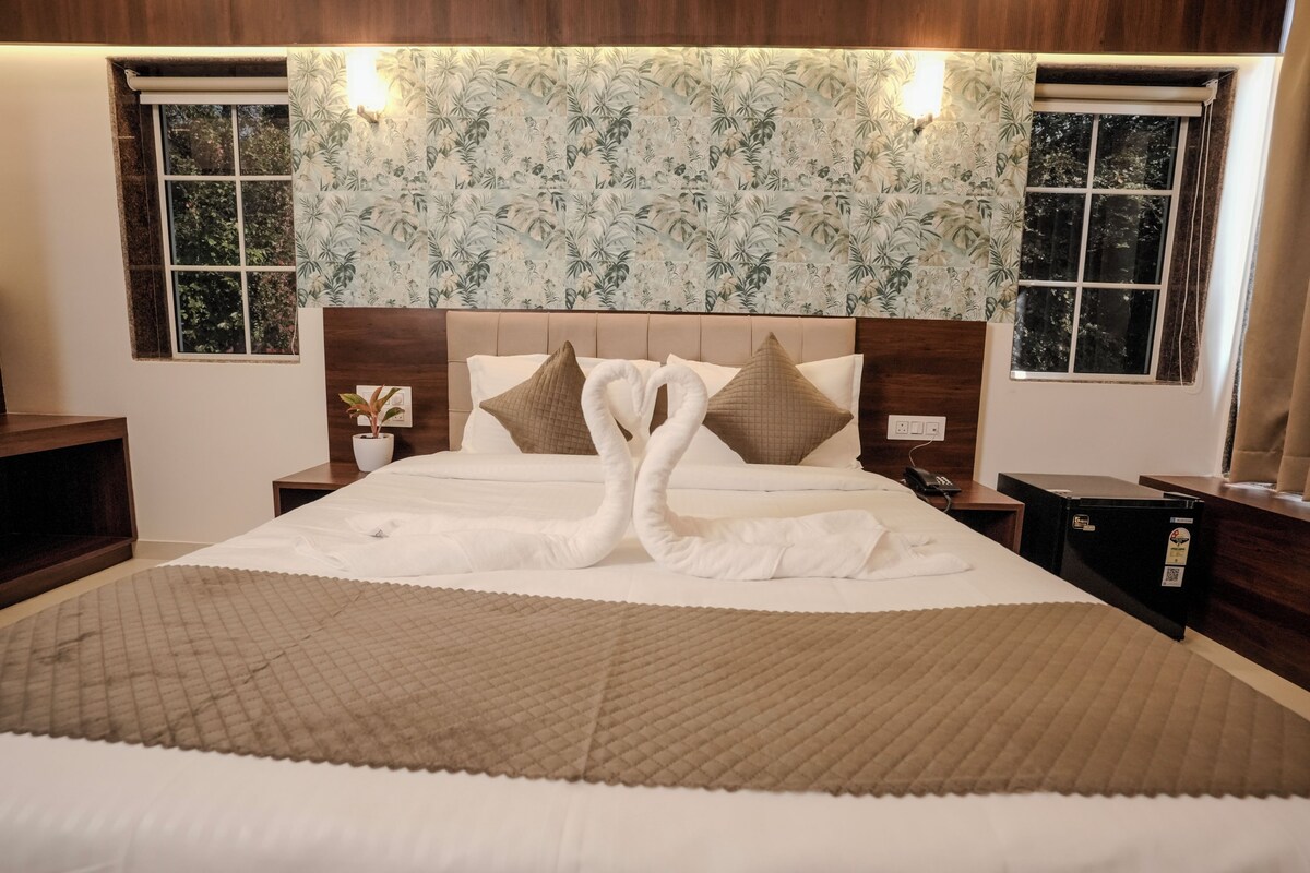 A hotel room with a large bed, two nightstands, a headboard with a floral pattern, and a window with a view of trees.
