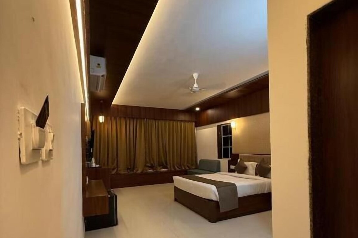 A modern hotel room with a large bed, a smaller seating area, a ceiling fan, and a view of the outdoors.