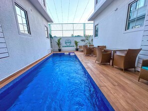 An indoor swimming pool with a wooden deck, wicker furniture, and a sign for High Five Hotels. - High Five Hotels (Assagao)