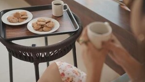 A person seated by a window with a table holding a plate of cookies and a cup. - High Five Hotels (Assagao)