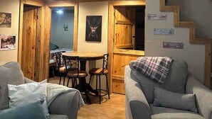 Un intérieur chaleureux avec deux canapés gris, une table à manger en bois avec des chaises, un escalier avec des rampes en bois et divers tableaux encadrés accrochés aux murs.