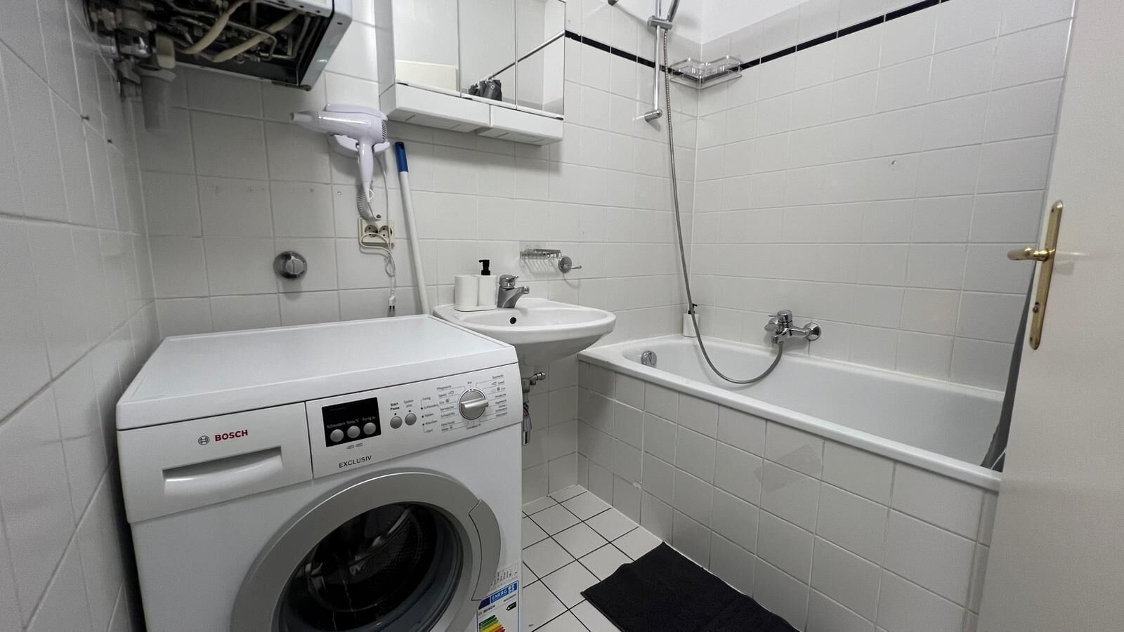 Ein kleines Badezimmer mit einer Waschmaschine von Bosch, einem Waschbecken und einer Badewanne.
