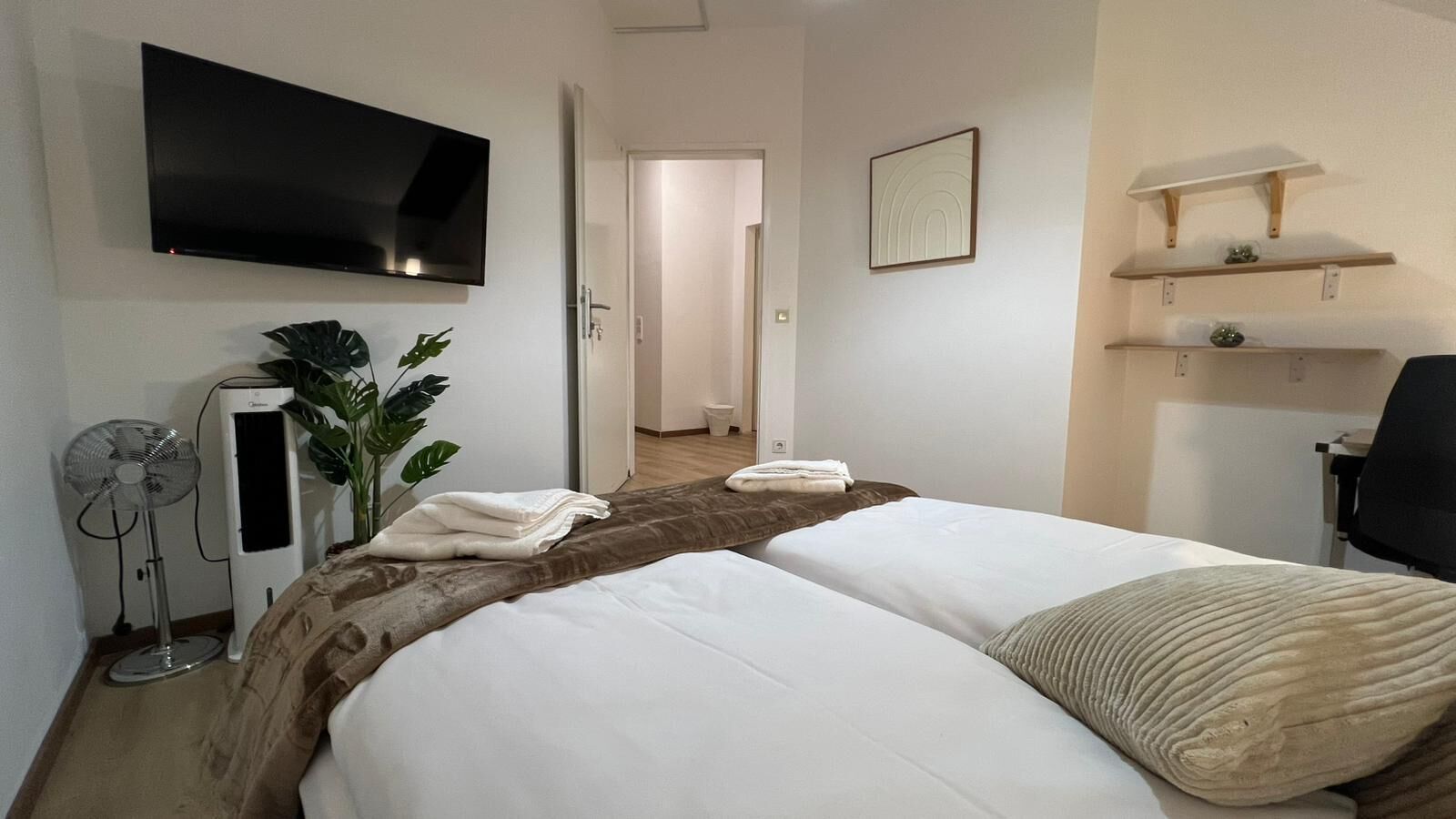 Ett hotellrum med två sängar, en TV, en fläkt och en växt.