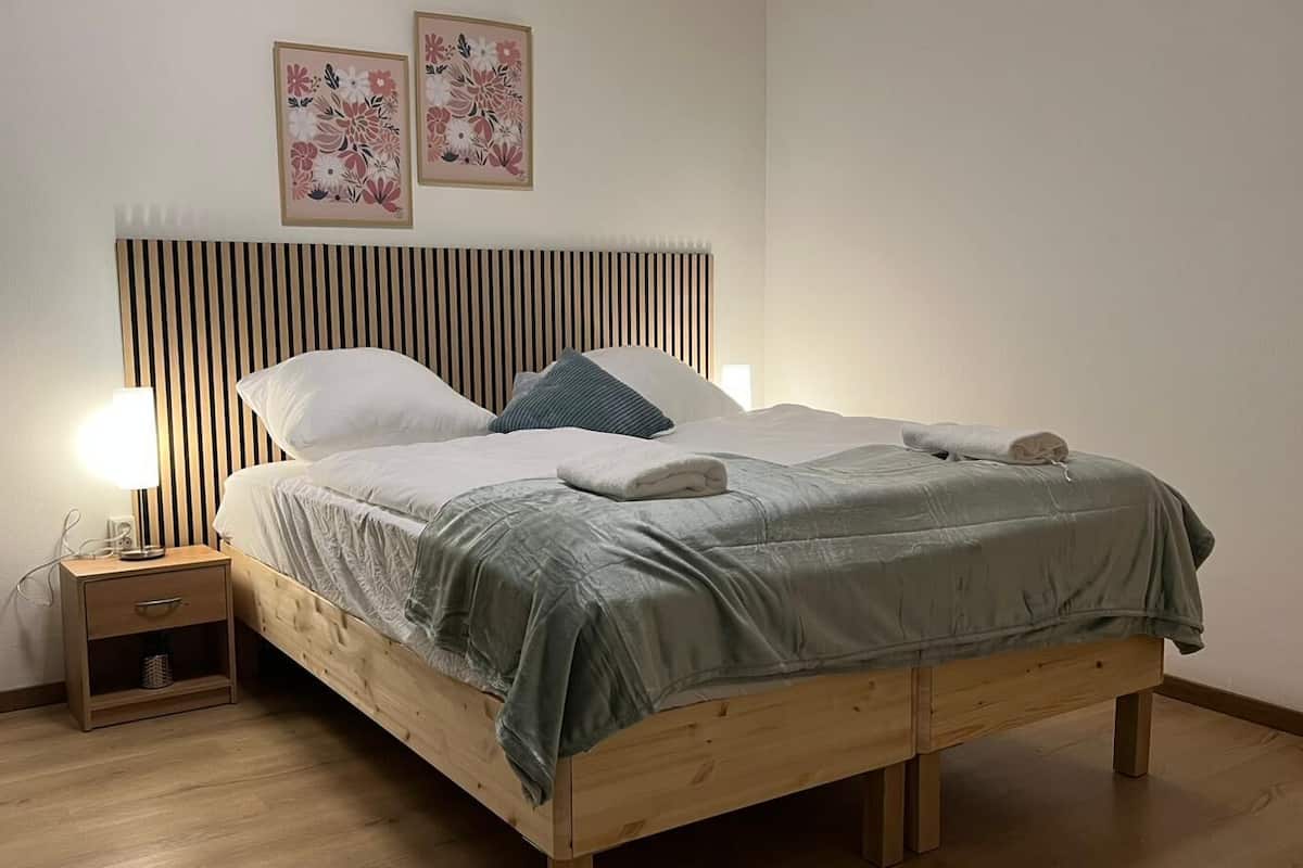 A neatly made bed with a wooden headboard, a bedside table with a lamp, and two floral wall art pieces.