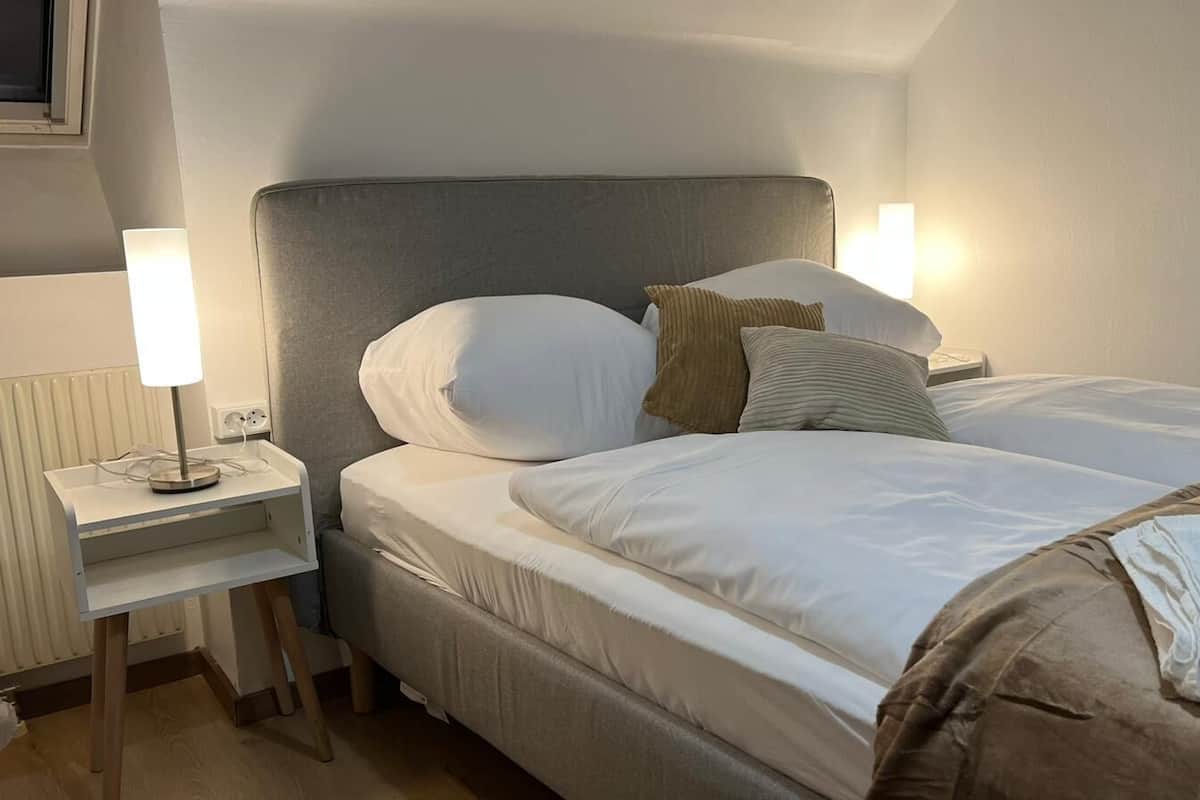 A hotel room with a bed, bedside table, lamp, and a radiator.