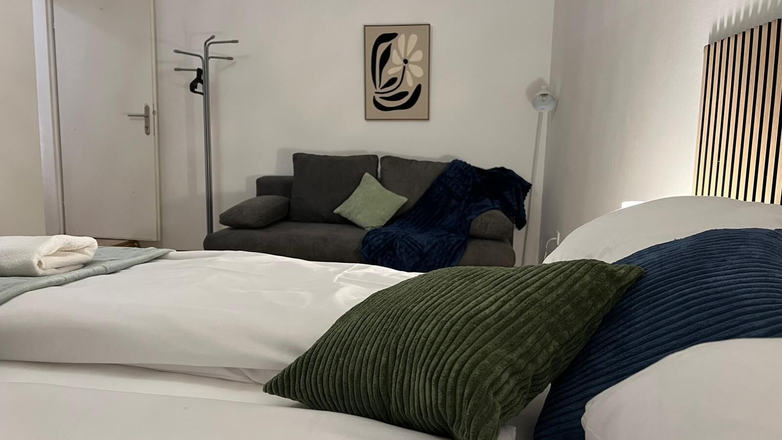 A bedroom with a bed, a grey sofa, and a wall-mounted artwork.