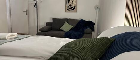 A bedroom with a bed, a grey sofa, and a wall-mounted artwork.