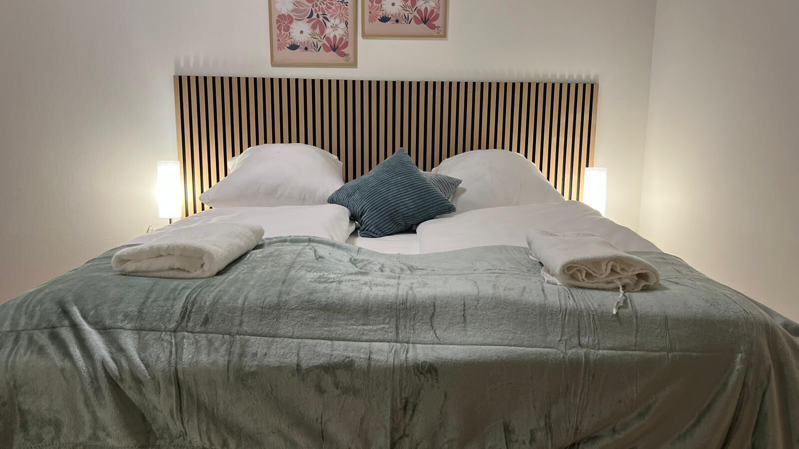 En snyggt bäddad säng med ett randigt sänggavel, två kuddar och en hopvikt handduk på varje sida.