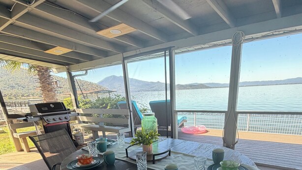 An outdoor dining area with a view of the lake and mountains, a grill, and a table set for two. - Cozy Lakefront Home with Amazing Lake Views from Huge Back Deck (Lucerne)