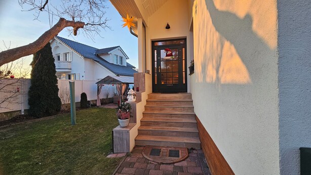 A house with a covered porch, a black front door, and a small staircase leading to the entrance. - Small apartment on the outskirts of Berlin (Teltow)