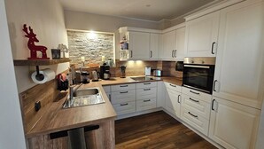A modern kitchen with white cabinets, a wooden countertop, a built-in oven, and a stone backsplash. - Small apartment on the outskirts of Berlin (Teltow)